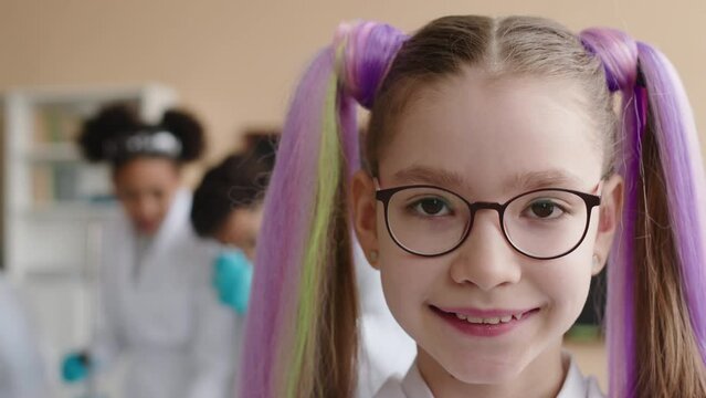 Medium closeup portrait of Caucasian preteen schoolgirl with long purple ponytails smiling at camera standing in Chemistry class during lesson