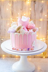 Princess pink cake with fondant crown, cotton candy, macarons, popsicles and ake pops on festive background