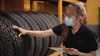 Worker young asia woman wearing face medical mask is checking quality of car tires and checking the...