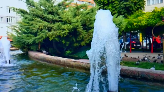Water stream with air bubbles from fountain on summer day, a small area with seating area, slow motion. Rest on street in evening after work, relaxation, communication, walking