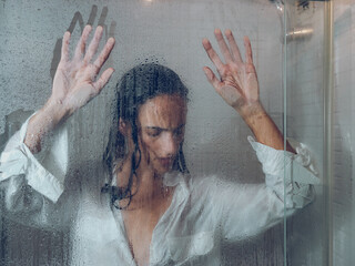Unhappy woman near misted glass door in shower
