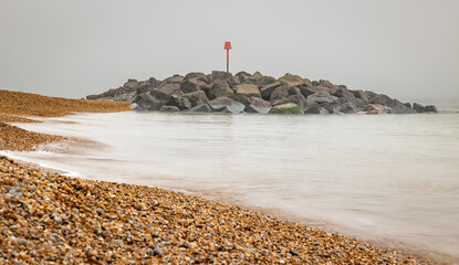 Rocky outcrop protecting a shingle beach with grey sky and grey sea at Hurst Spit, Keyhaven, Hampshire UK
