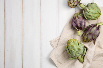Fresh green and purple artichokes on tray on white wooden background
