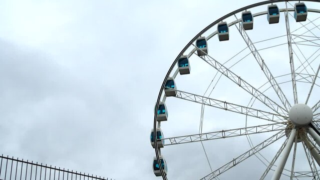 The ferris wheel is spinning slowly against the background of a cloudy sky.
