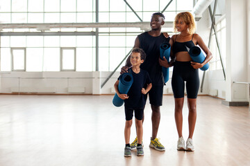 Fototapeta na wymiar african american young family stands together in the gym and holds yoga mat, father mom and son on fitness training