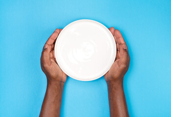 Man holding an empty white plate isolated on blue background, top view