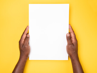 Man holding a blank sheet of paper on yellow background, top view
