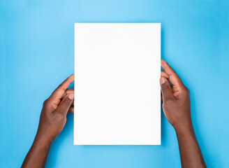 Man holding a blank sheet of paper on blue background, top view