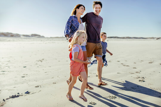 Young caucasian family walking on a sandy beach during their summer vacation - Powered by Adobe