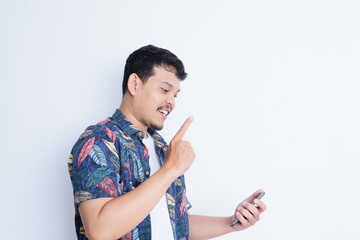 Adult Asian man wearing beach shirt looking to his phone while pointing to the right direction