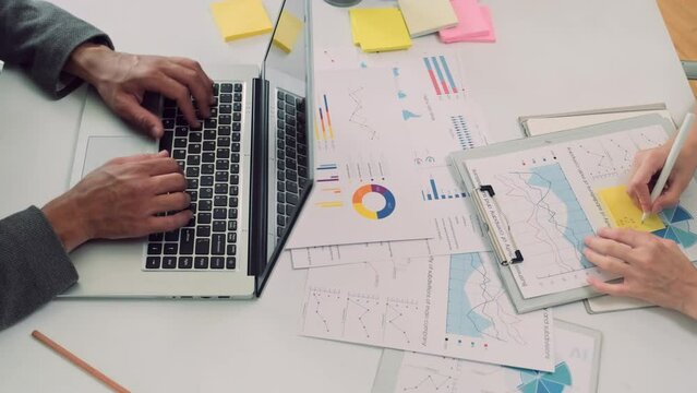 Top down view of entrepreneurs working at business charts while developing business strategy, writing something on sticker