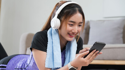 Young asian woman lying on floor to surfing internet and listens music on smartphone after exercise