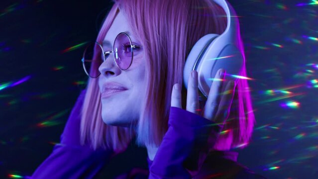 Beautiful woman in futuristic costume over white background. Violet neon light. Portrait of young girl in modern headphones listening music.