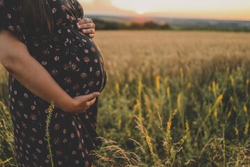 Close-up of pregnant woman with hands on her belly on nature background. Concept of pregnancy, maternity, expectation for baby birth