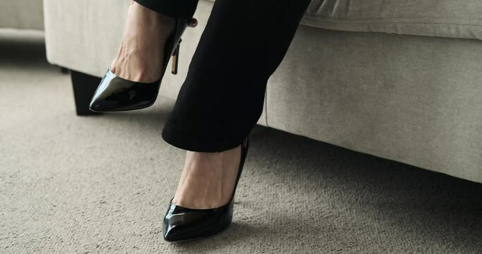 A close-up shot of a businesswoman's feet as she takes off her shoes and comfortably lays down on a sofa to unwind. The scene captures her gesture of relaxation after a busy day at work.
