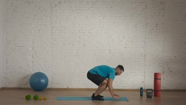 Man fitness trainer in sportswear doing burpee with high jumps exercise for online class at home studio.