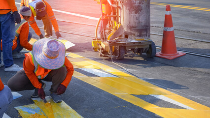 Road workers with thermoplastic spray road marking machine are working to paint traffic yellow...