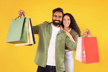 Happy middle eastern spouses holding colorful shopper bags, yellow background