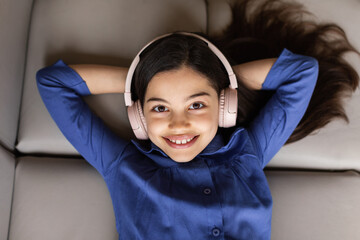 Cheerful kid girl listening music wearing wireless headphones at home