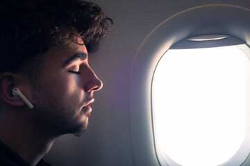 Jeune homme dormant dans un avion. Homme assoupi contre un hublot. Voyage tranquille en avion. Sérénité du passager de l'avion. Ecouter de la musique en avion