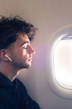 Jeune homme dormant dans un avion. Homme assoupi contre un hublot. Voyage tranquille en avion. S&eacute;r&eacute;nit&eacute; du passager de l'avion. Ecouter de la musique en avion