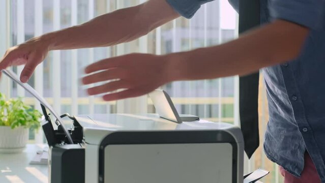 Hands of male office manager putting paper to printer when preparing to conference indoors