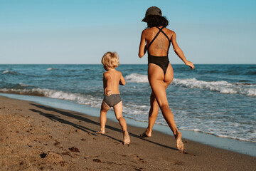 Fototapeta premium beautiful sports mom runs with her son along the seashore on the beach