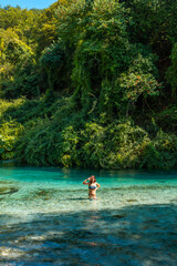  Woman tourist bathing smiling in the cold waters of the river of The Blue Eye or Syri i kalter in the mountains of southern Albania, vertical photo