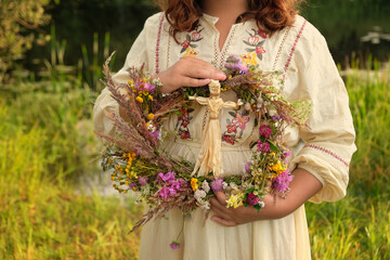 wreath of flowers and corn doll in hands girl outdoor, natural background. Magic ceremonial, symbol of harvest. witch tradition, wiccan ritual. decor for Midsummer, Litha, Lammas or Lughnasadh sabbat - obrazy, fototapety, plakaty
