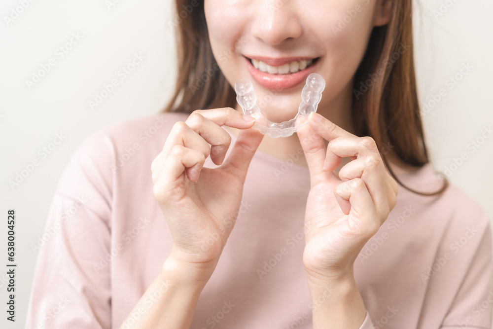 Wall mural Dental invisible braces, beautiful smiling asian young woman holding invisalign braces, wearing orthodontic silicone trainer, white smile using invisible whitening tray. Stomatology, dental healthcare