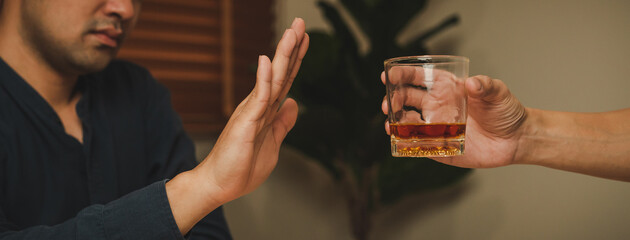 Alcoholism, sad depressed asian young man refuse, push alcoholic beverage glass, drink whiskey, sitting alone at night. Treatment of alcohol addiction, having suffer abuse problem alcoholism concept.