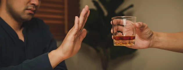 Fotobehang Alcoholism, sad depressed asian young man refuse, push alcoholic beverage glass, drink whiskey, sitting alone at night. Treatment of alcohol addiction, having suffer abuse problem alcoholism concept. © KMPZZZ