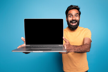 Great website. Excited middle aged indian man holding laptop computer with blank screen and...