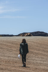 Woman walking on volcanic area with white cap in her hand with lunar landscape 