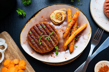 Grilled vegan plant-based meat with carrots on a plate on the black table.