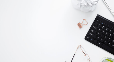 Workplace with white notebook, black keyboard, stationery, glass of water with lime and glasses on white desk. Flat lay office desk, mock up space for text. Top view. Copy space