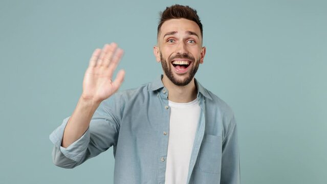 Young man wear shirt white t-shirt look around for friend find waving meet greet with hand as notices someone say hello hi isolated on plain pastel light blue cyan background. People lifestyle concept