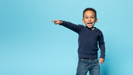 Funny african american boy pointing aside at copy space, emotional male child demonstrating free place for ad