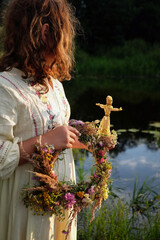 Girl with floral wreath and corn doll in hands outdoor, natural background. Magic ceremonial, symbol of harvest. witch tradition, wiccan ritual. decor for Midsummer, Litha, Lammas or Lughnasadh sabbat