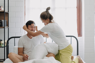 Asian wife and husband playing pillow fight funny and laugh on the bed.
