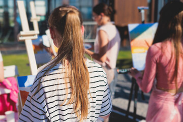 Process of drawing, group class of talented students with painting easels and canvases during lesson of watercolour painting outdoors, drawing class for adult artists in art school