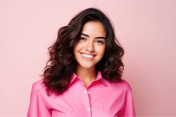 Smiling attractive young hispanic woman wearing a pink shirt on a light cream background looking at the camera
