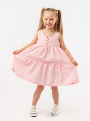 Naklejka premium A 5-year-old Caucasian girl with long hair stands on a white background smiling, holding a pink dress with her hands. The legs are crooked.