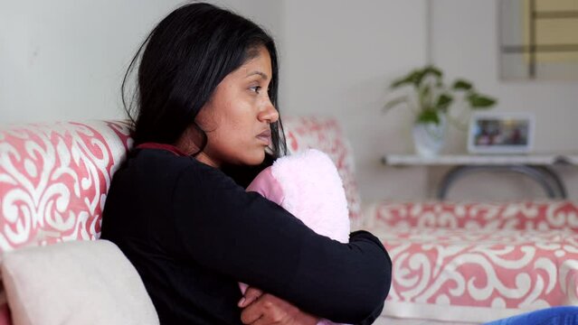 Sad woman hugging pillow on sofa