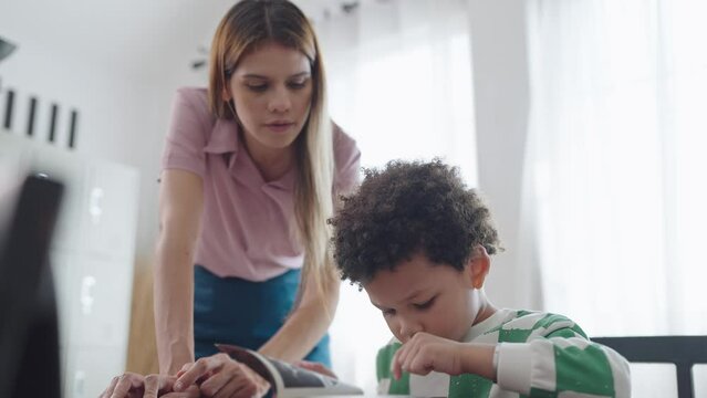 Female teacher helping little African American boy reading a book at school. kindergarten woman teacher talking and explaining with little school boy reading a book. Education and learning concept 