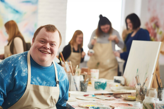 Young smiling man with Down syndrome on art workshop with a group of students, learning a new skill. Social integration concept.