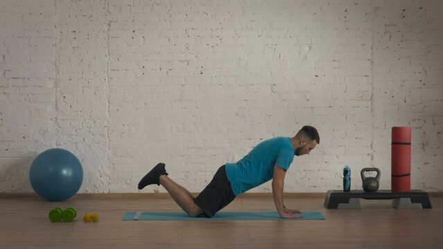 Man fitness coach in sportswear doing knee push ups exercise for online class at the home studio.