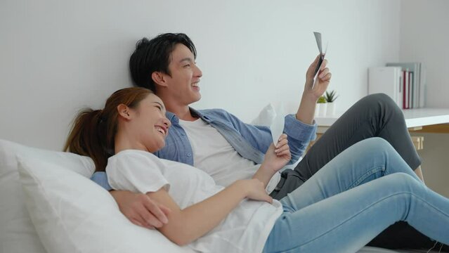Asian couple lying down looking at the ultrasound results of their baby in the bedroom, concept of initiation, family relationship
