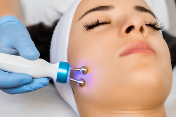 Application of microcurrent massage device on female face by cosmetologist. 