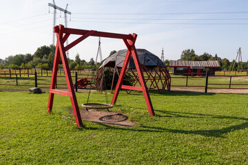 Red big wooden swing in a meadow with green grass. Sunny summer day